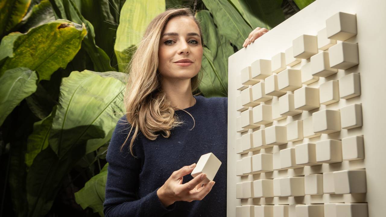 Bianca Caloi Di Grassi posa ao lado de quadro branco com cubos grudados.