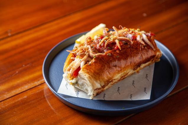 Calamari roll: sanduíche recheado de lula fresca salteada com bacon caramelado, tomate-cereja, cebola-roxa, uva verde e páprica no pão de cachorro-quente