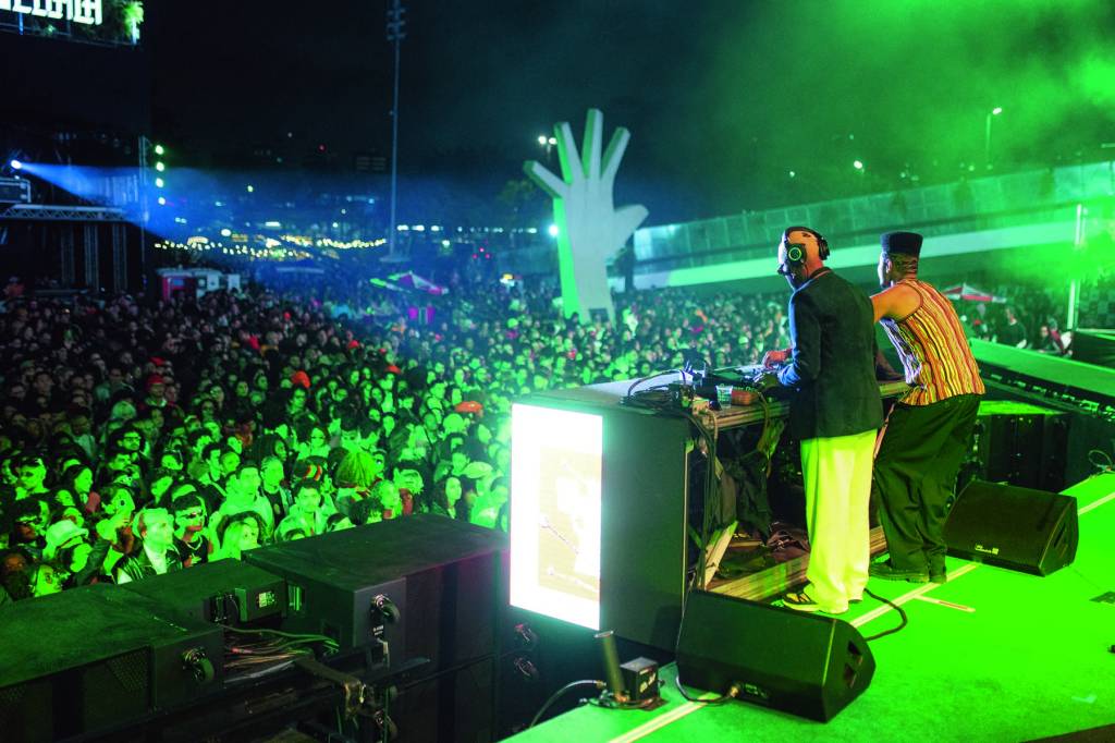 Imagem mostra dois DJs atrás de mesa de som em frente a multidão