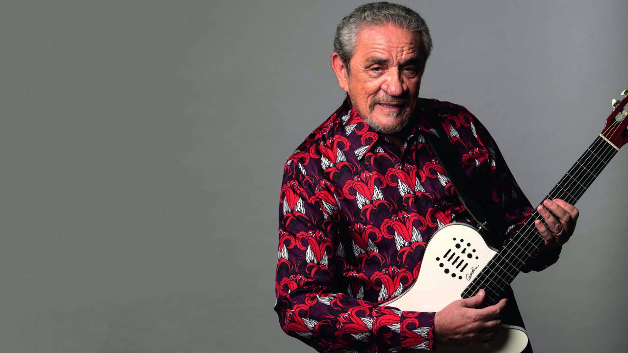 Imagem mostra homem de camisa tocando violão