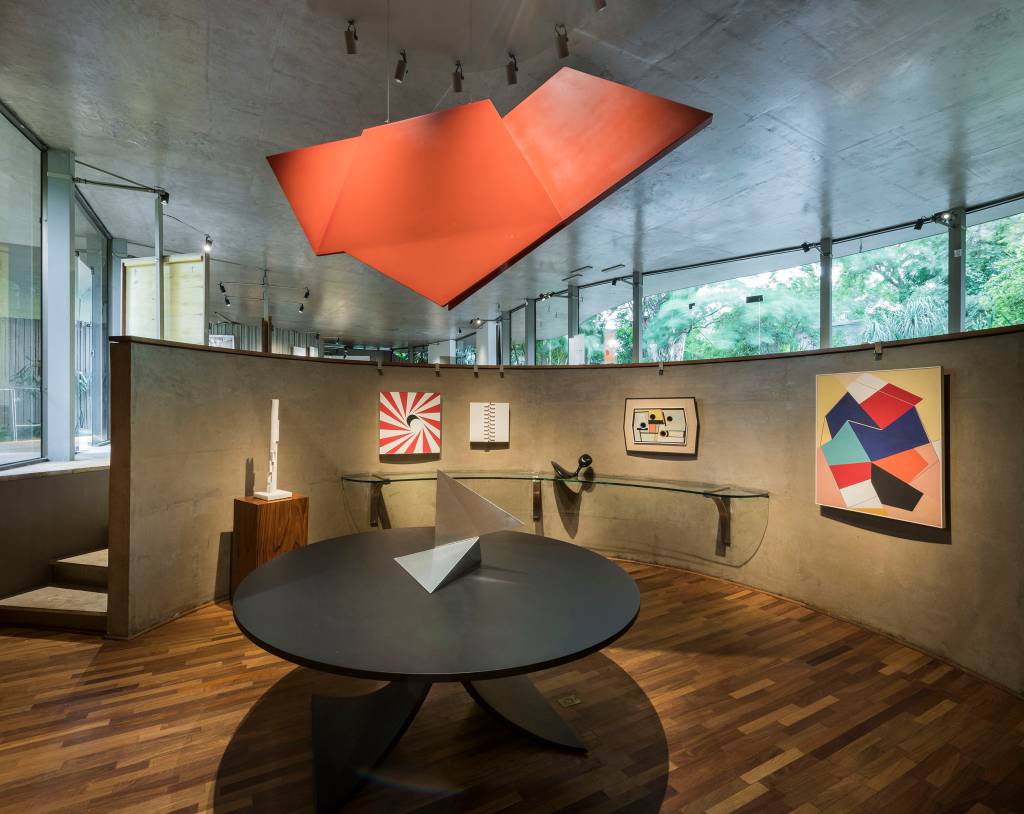 Obras dispostas na copa da casa projetada por Niemeyer. As paredes delimitam um formato circular e nelas estão quadros com abstrações geométricas coloridas. A obra 