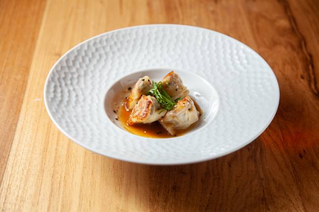 Prato branco de porcelana sobre mesa de madeira contendo dumpling com recheio de peixe ao molho de missô