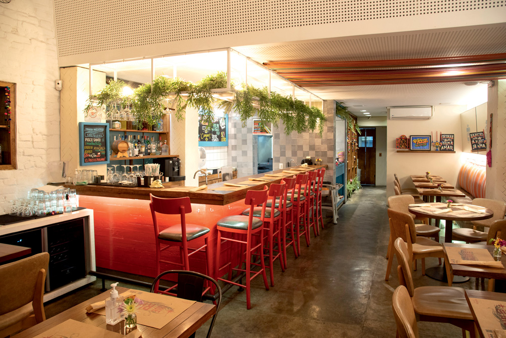 Imagem mostra ambiente de restaurante, iluminado, com balcão de cadeiras vermelhas