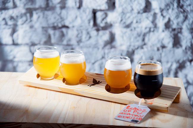 quatro copos em uma base de madeira contendo cervejas de cores diferentes