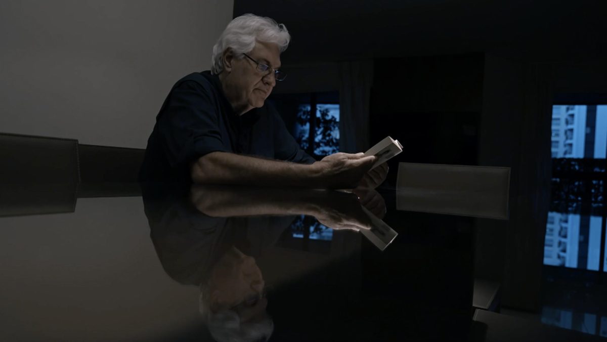 Homem de óculos lê livro em uma mesa