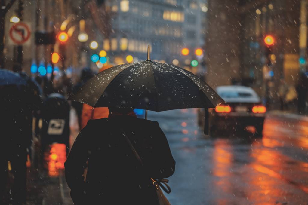 homem andando com guarda-chuva na rua de uma cidade à noite