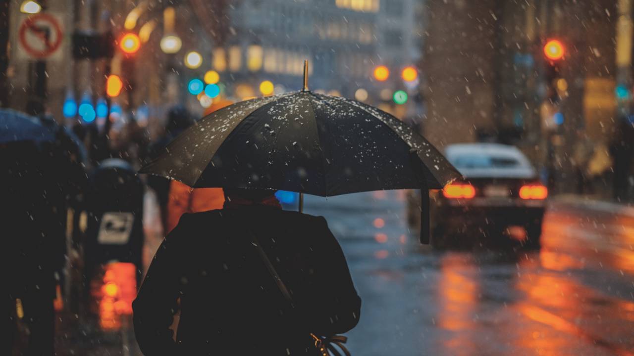 homem andando com guarda-chuva na rua de uma cidade à noite