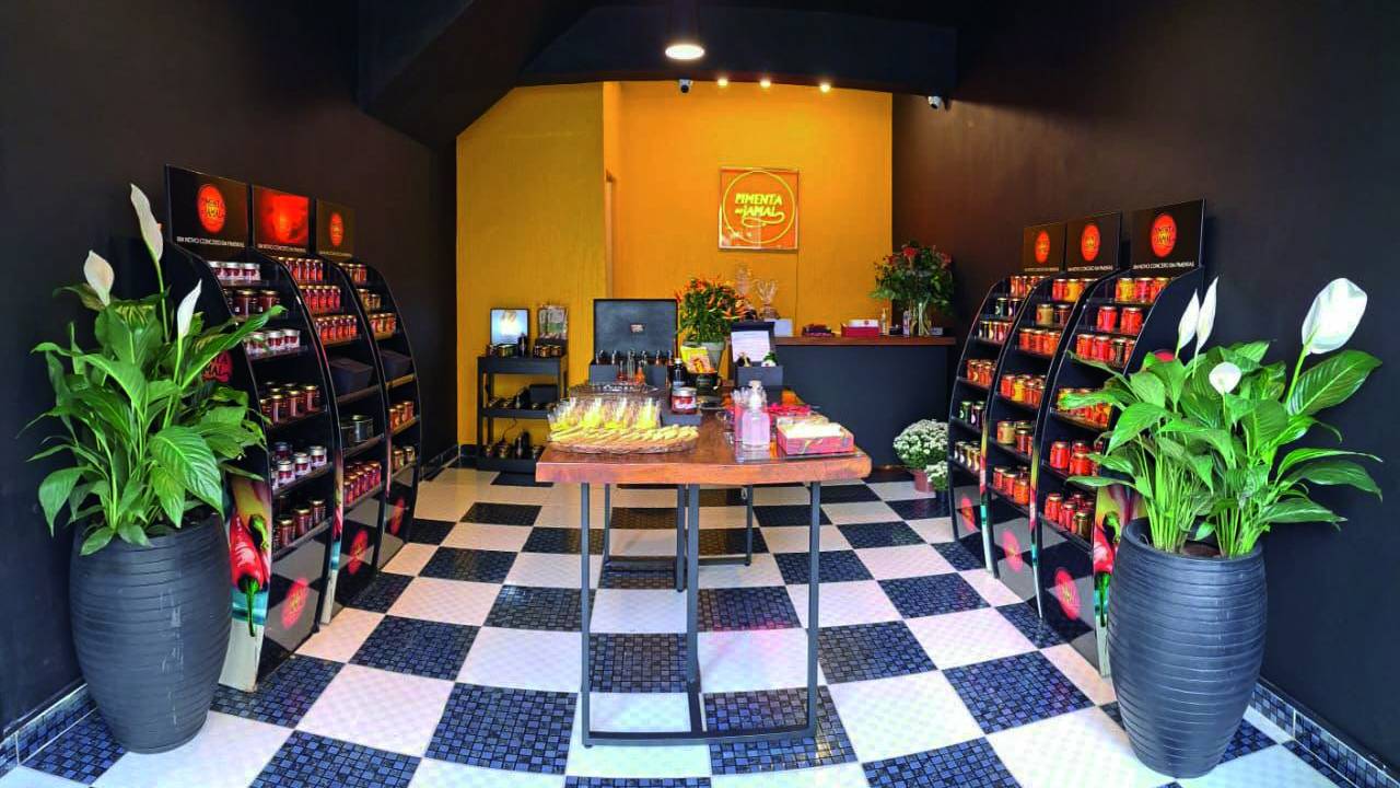 Imagem interna de loja com chão quadriculado, parede amarela ao fundo e dois estandes nas laterais contendo os produtos