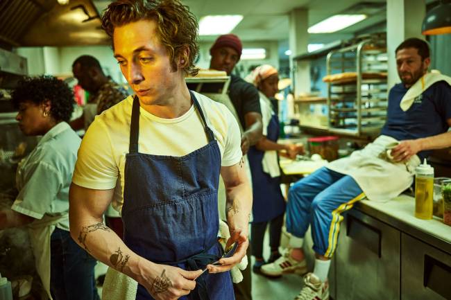 Chef à frente da cozinha de seu restaurante, com equipe ao fundo