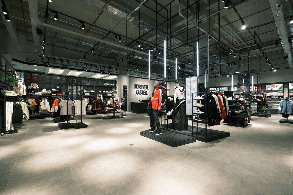 Foto exibe interior de loja da Puma com círculos de luz no chão cinza e manequins vestidos ao fundo.
