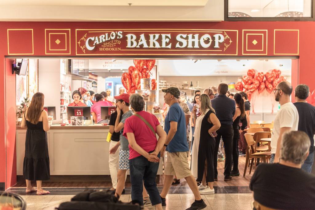 Fachada exibe título Carlo's Bakery Shop com pessoas paradas na porta.