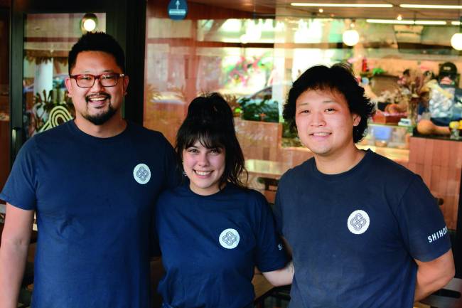 Dois homens e uma mulher vestindo o uniforme do Pasta Shihoma sorriem para a câmera