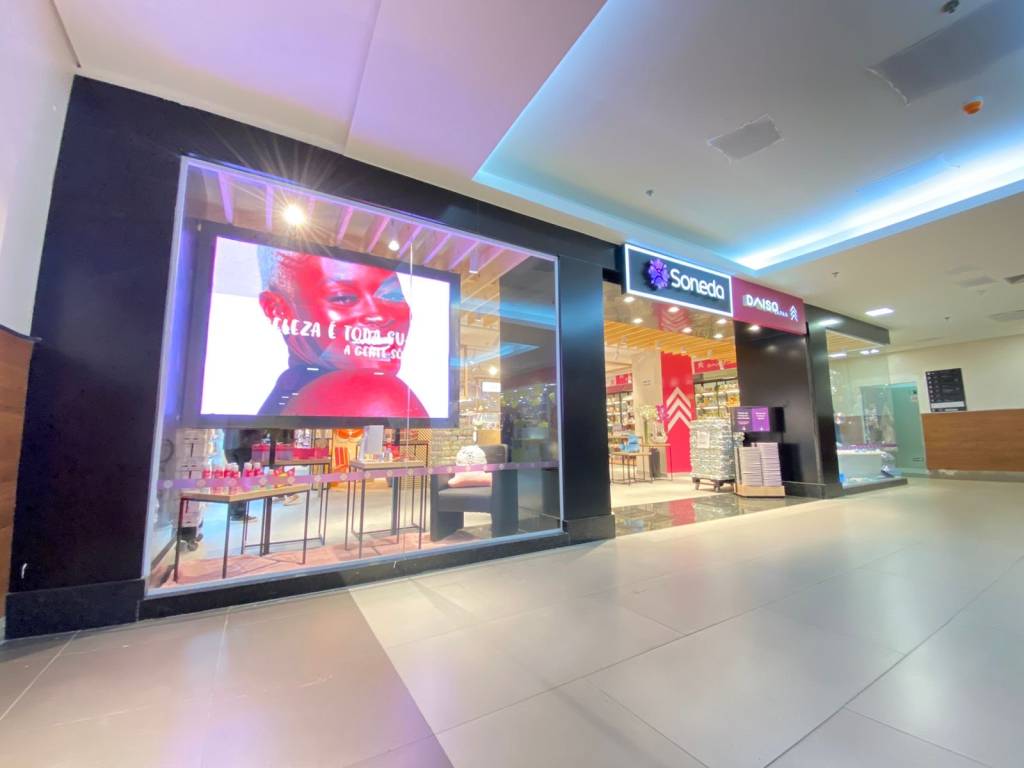 Imagem exibe vitrine de shopping com telão iluminado e placa 
