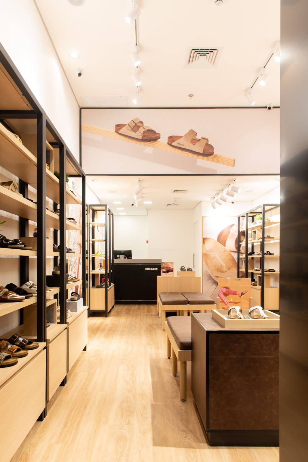 7 – Birkenstock (Divulgação) (1) Foto vertical exibe prateleiras com sandálias de couro nas laterais e caixa ao fundo. No topo, uma grande imagem de um par de sandálias.