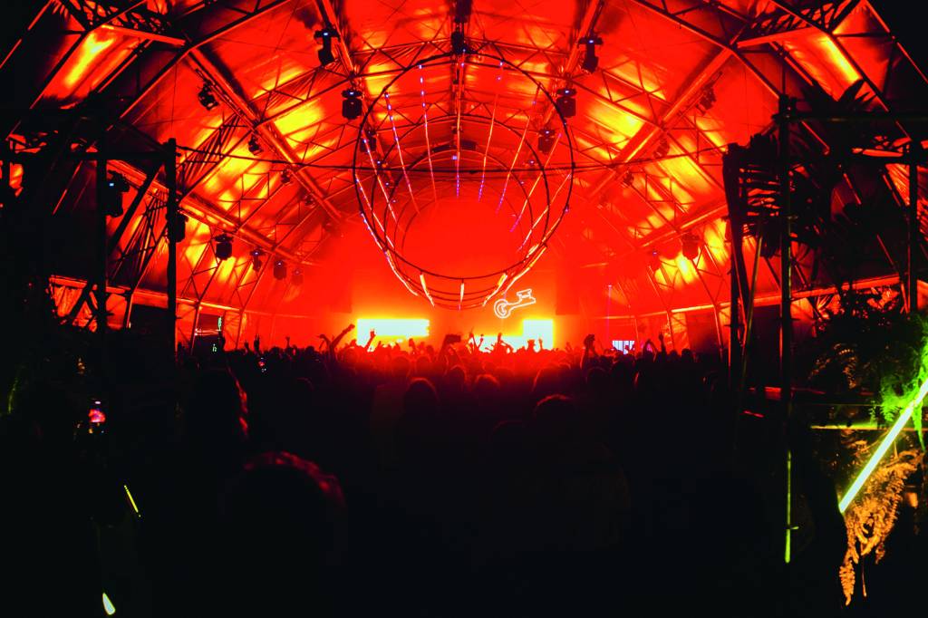 Imagem mostra espaço com luzes laranjas e multidão