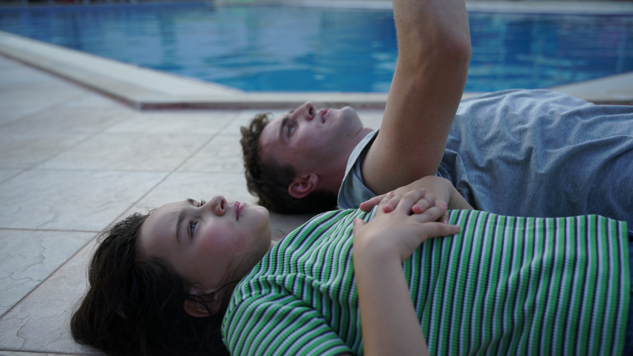 Homem e menina deitados à beira da piscina