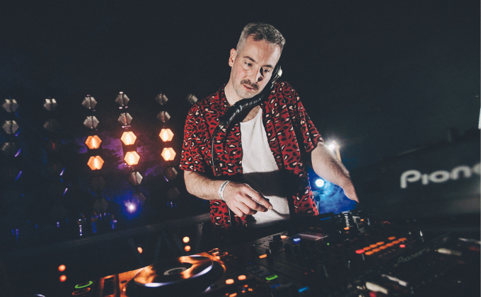 Imagem mostra DJ de camisa estampada tocando em palco