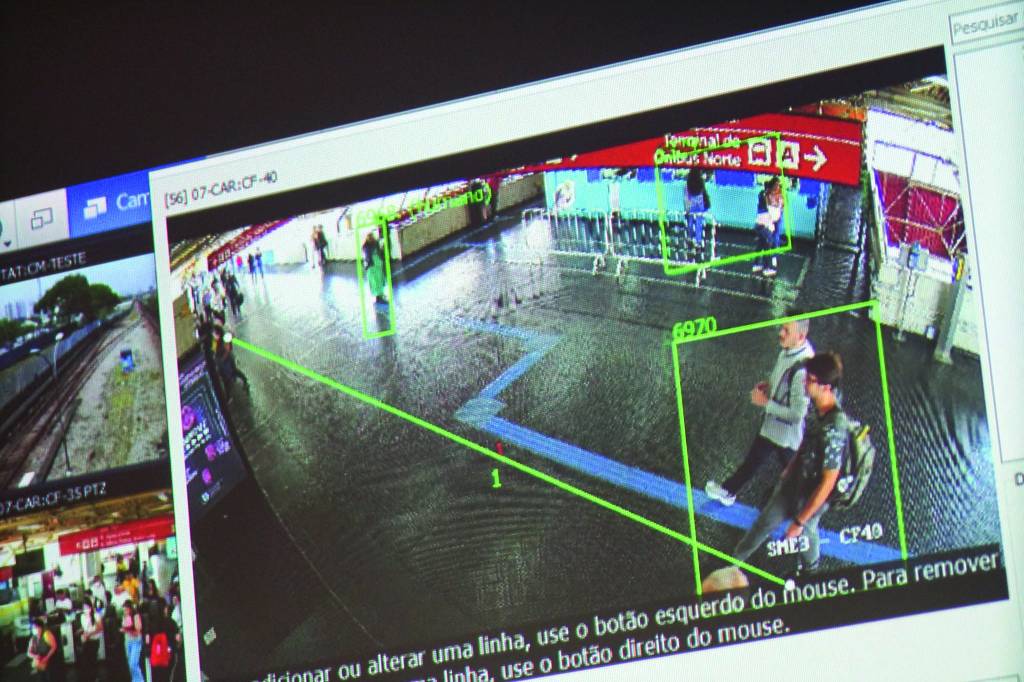 Imagem de câmera de monitoramento no metrô. Foca em dois homens andando