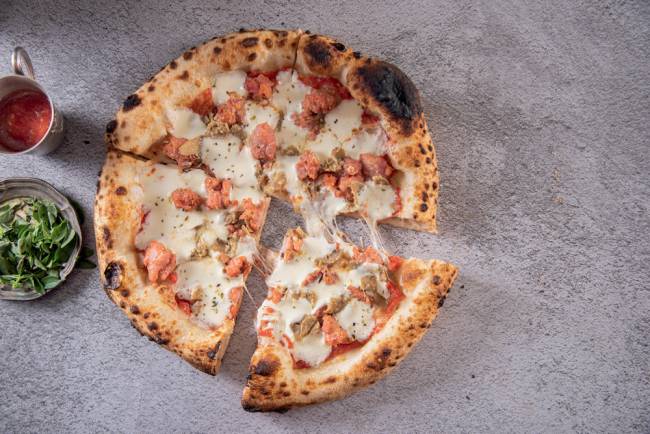 Pizza sobre superfície de pedra cortada em 4 pedaços, com um deles um pouco afastado dos demais
