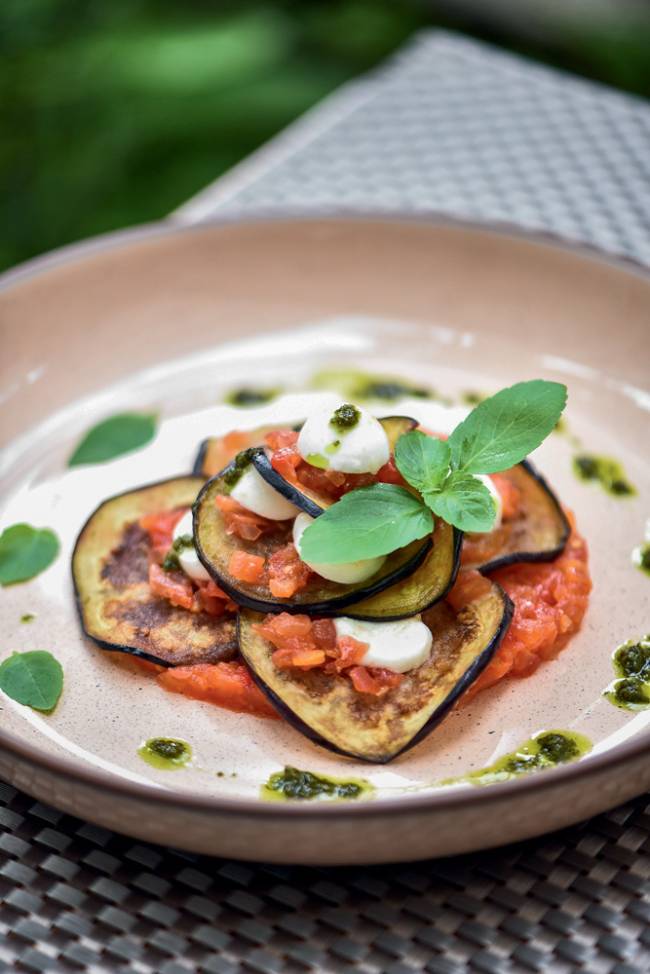 Prato de cerâmica com rodelas de berinjela com molho de tomate, mussarela de búfala e folhas de manjericão