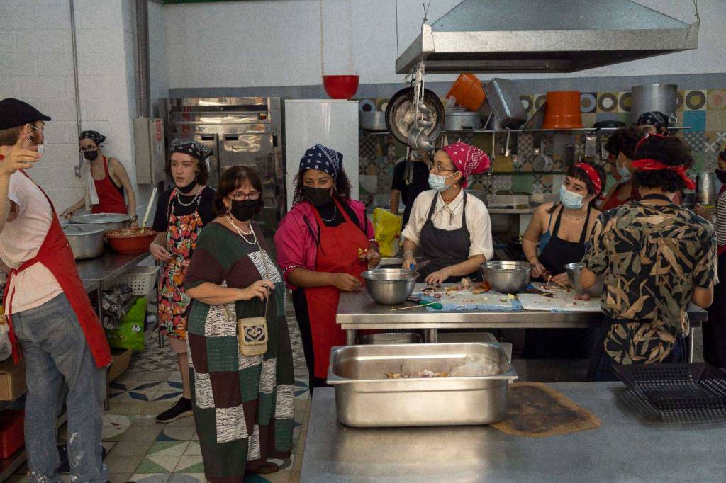 Alunos com máscaras preparando churrasco na cozinha da escola