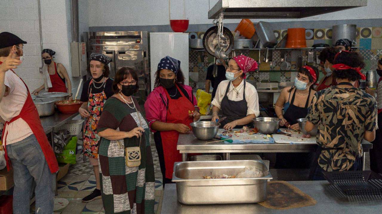 Alunos com máscaras preparando churrasco na cozinha da escola