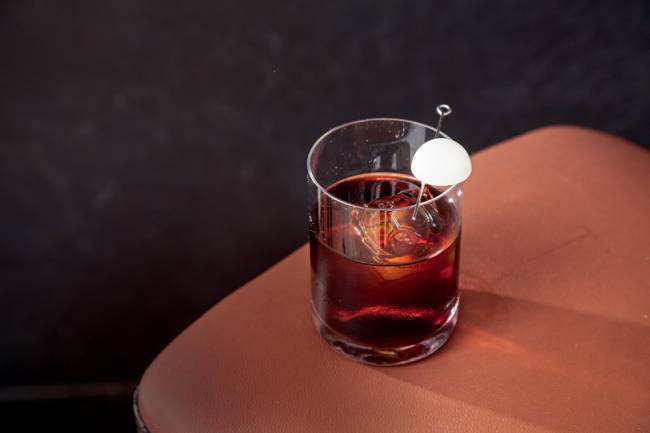 Moccha santana bar Copo baixo com conteúdo marrom-avermelhado e um bombom branco sobre mesa de madeira