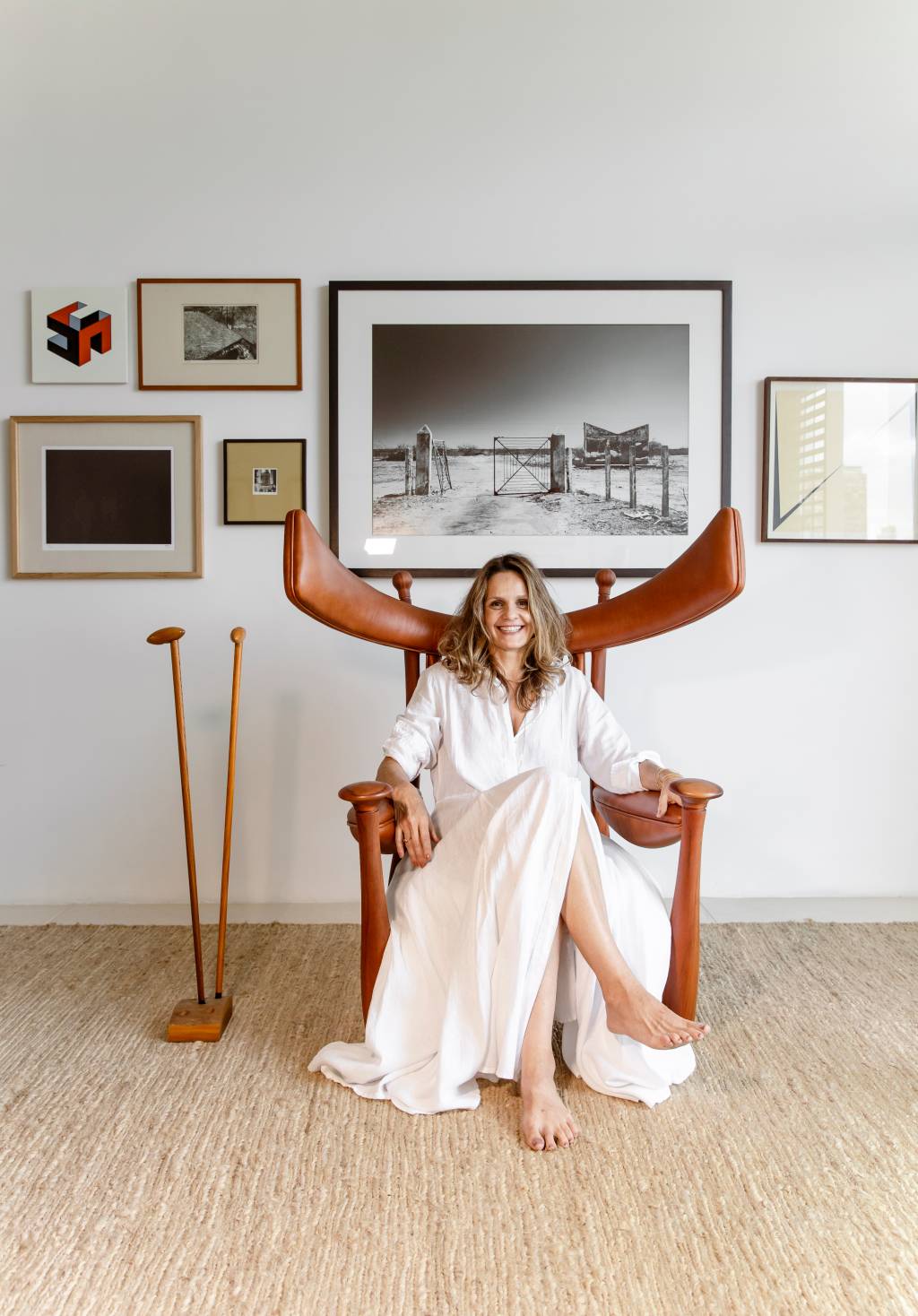 Renata Aragão (Flora Negri-Divulgação) Renata Aragão posa sentada em cadeira com pontas avantajadas de madeira. Veste vestido todo branco, tem cabelos claros longos. Ao fundo, quadros em diversos tamanhos exibem paisagens.