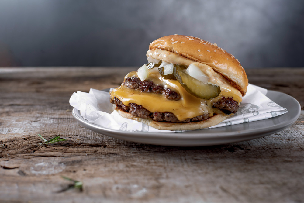 Hamburguer sobre prato com dois discos de carne cebola e picles