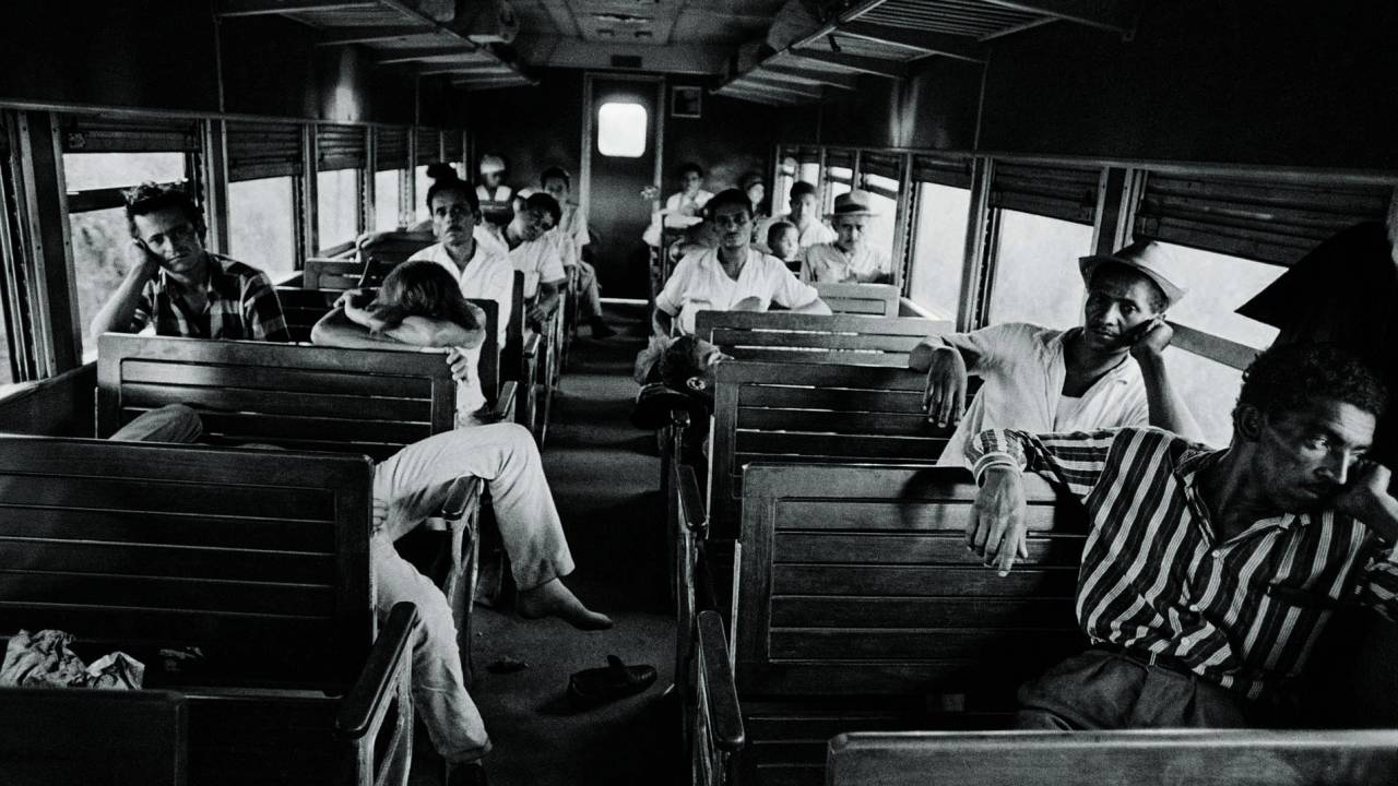 Imagem em preto e branco mostra interior de trem com diversos homens deitados nos bancos