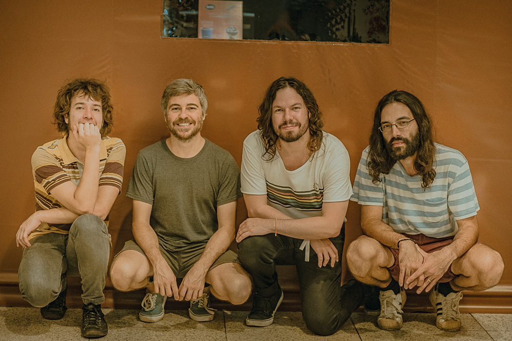 Imagem mostra quatro homens agachados, sorrindo