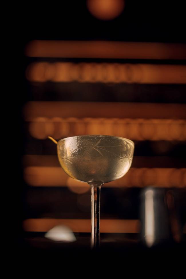 fel Pavillon royal Taça alta e arredondada com padrão gravado, líquido claro e translúcido, com luzes indicando prateleiras de bar ao fundo