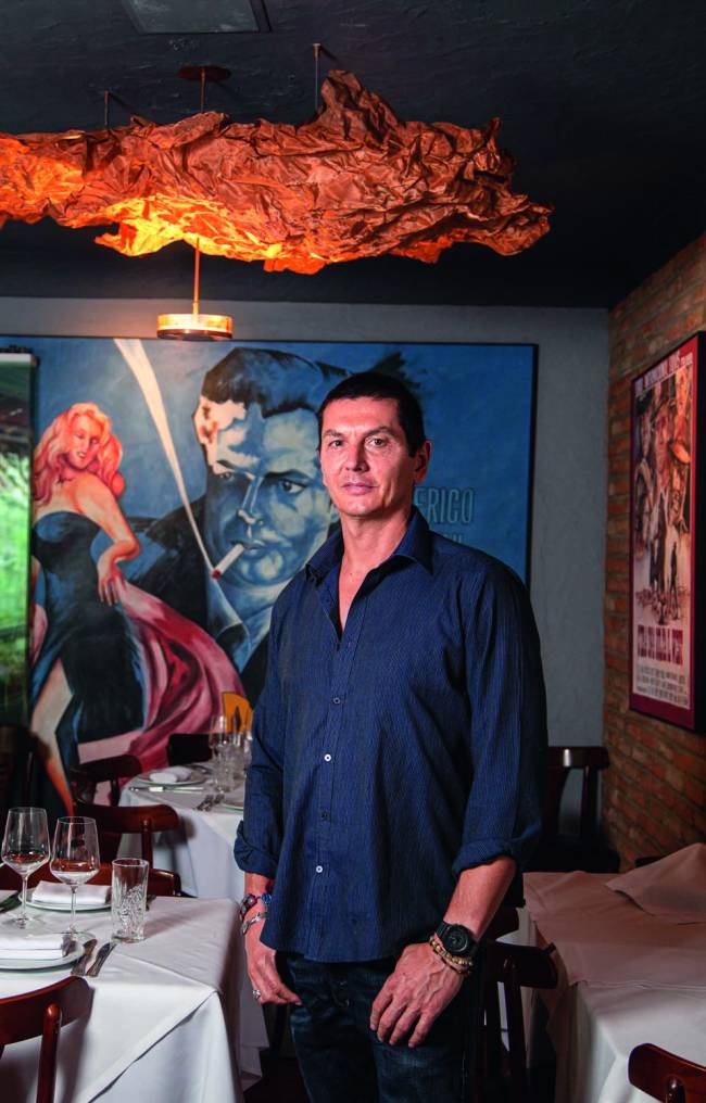Homem de camisa azul escura em ambiente interno em frente a um quadro