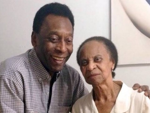 Foto de Pelé e Dona Celeste sorrindo, eles estão sorrindo, o fundo é uma parede branca