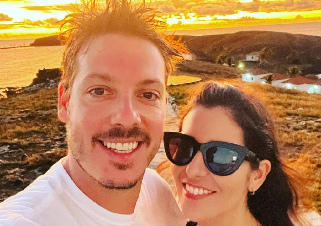 Fabio Porchat e Nataly Mega sorrindo juntos, com por do sol ao fundo.