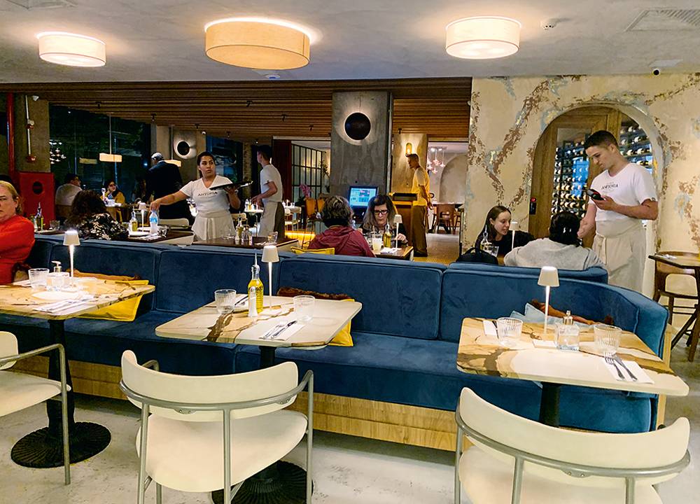 Área interna de restaurante com banco estofado azul e cadeiras brancas