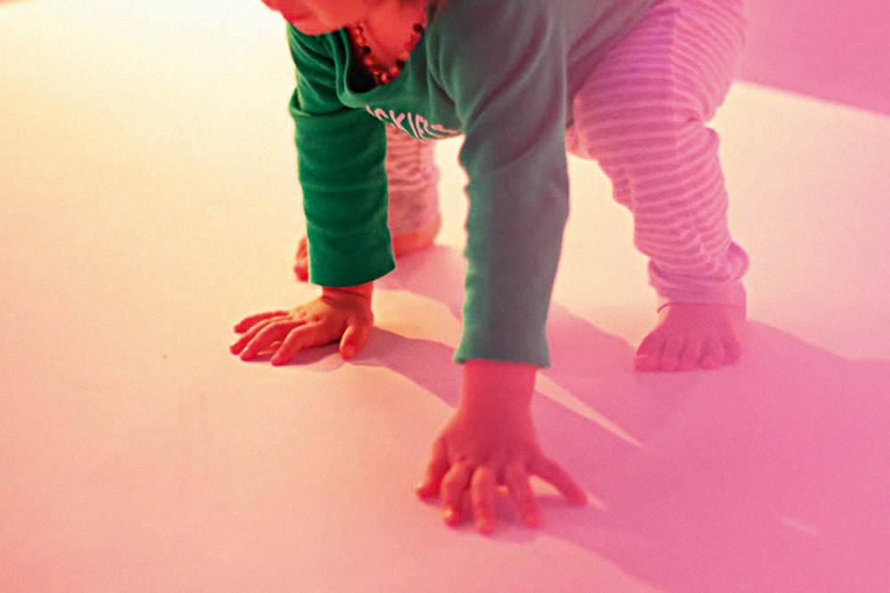 Bebê apoia as mãos e os pés no chão. Seu rosto não aparece