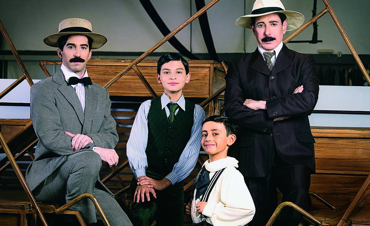 Mateus, Henrique, Felipe e Cassio (a partir da esquerda) posam caracterizados como Santos Dumont, os dois da ponta mais velhos e com chapéus claros. Os dois do meio são crianças, também com roupas antigas, camisas branca e azul, e coletes escuros.