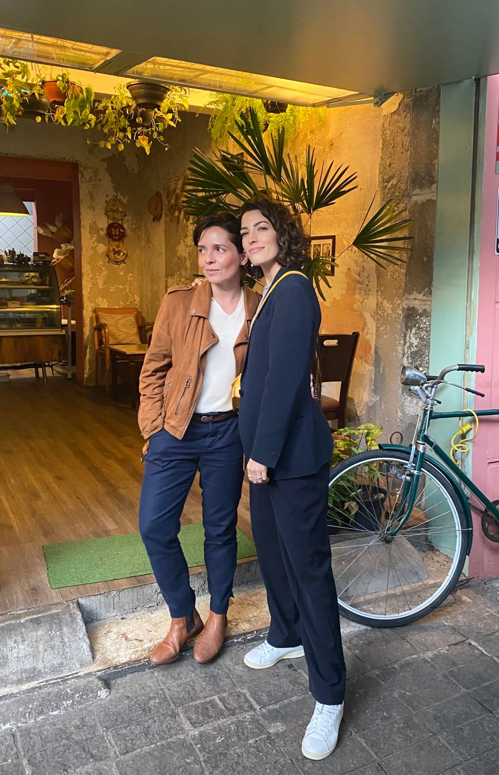 Nadia e Sílvia (ACERVO PESSOAL) (2) Nadia Bochi e Sílvia Henz posam de pé abraçadas, ambas com calças escuras, Silvia à direita com blazer preto e Nadia com camisa branca e jaqueta marrom. Ao lado aparece uma bicicleta.