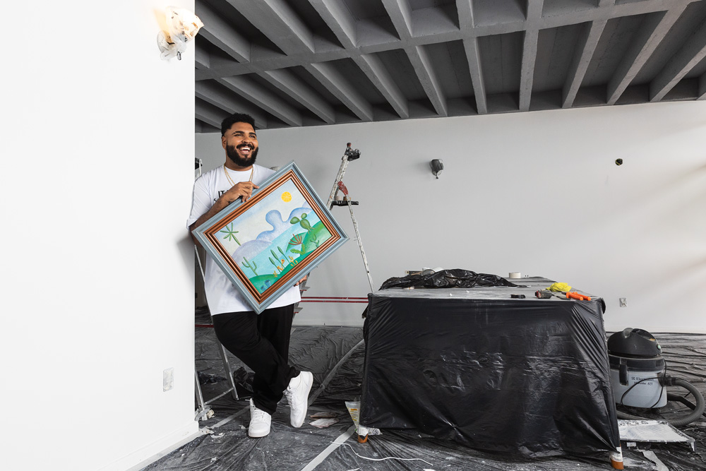 Paulo Vieira Imagem mostra homem sorrindo, apoiado em parede, segurando quadro de Tarsila do Amaral