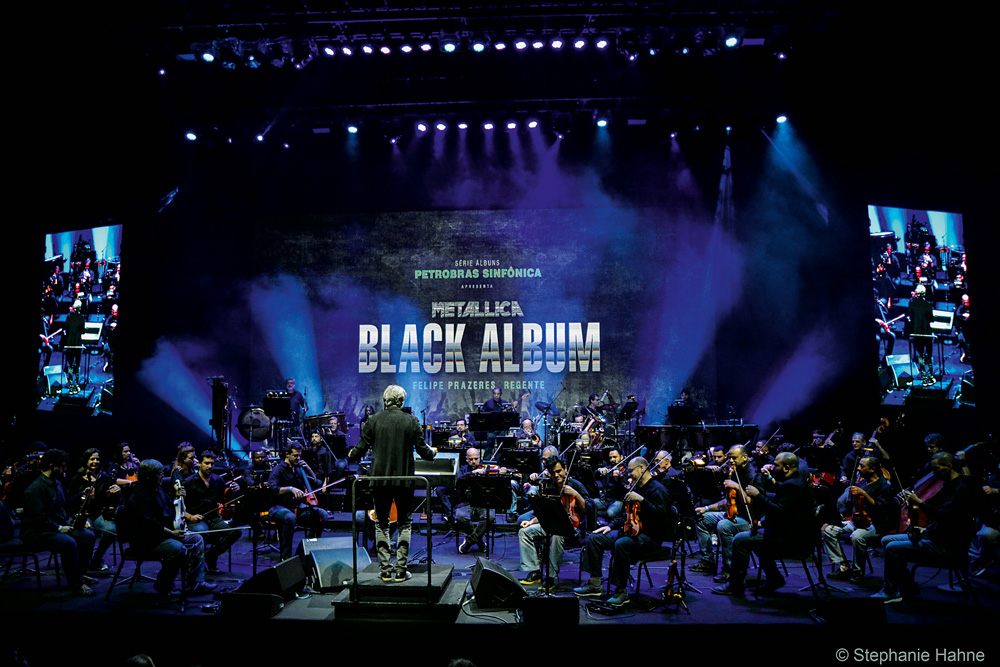 Imagem mostra orquestra em palco, com luzes azuis