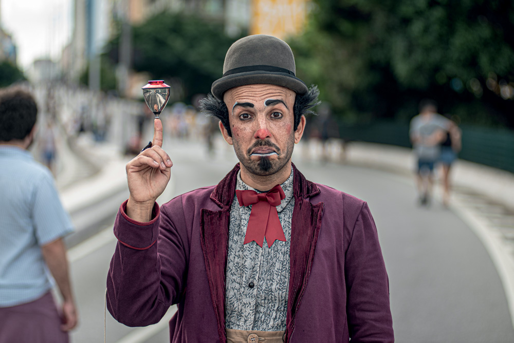 Palhaço Matias Donoso equilibra um pião no dedo indicador no meio da Avenida Paulista