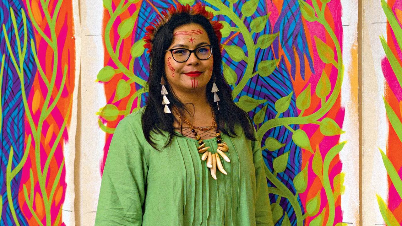 Foto mostra Daiara Tukano, uma mulher indígena, em frente à pintura colorida