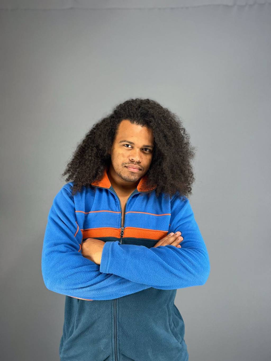 David Costa (David Costa-Divulgação) Homem negro com cachos grandes encara a câmera com braços cruzados e veste suéter azul.