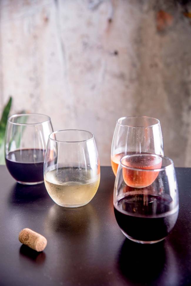 Quatro copos com vinhos distintos sobre mesa preta laqueada