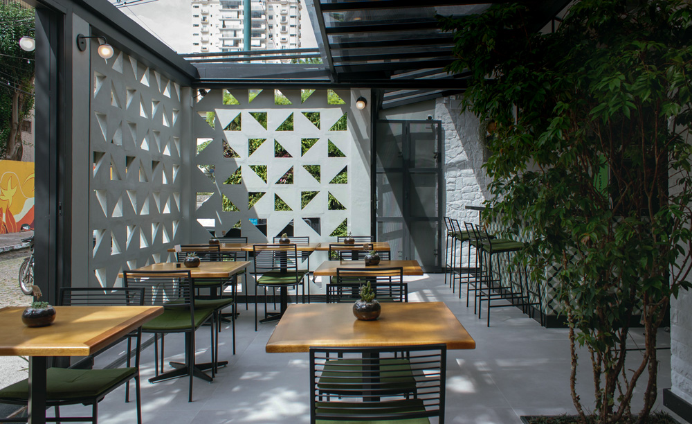 Ambiente externo green kitchen com mesas e mural com recortes