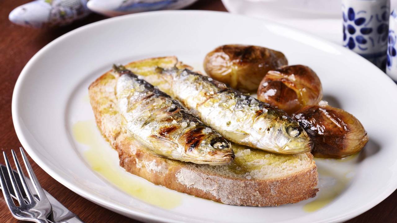 Prato branco de porcelana com fatia de pão, batatas e duas sardinhas