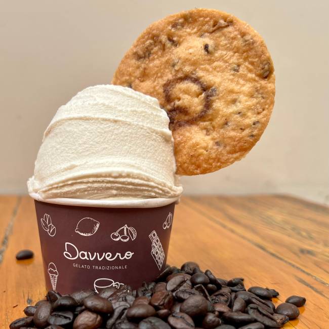 Potinho de sorvete com biscoito em cima e grãos de café na mesa