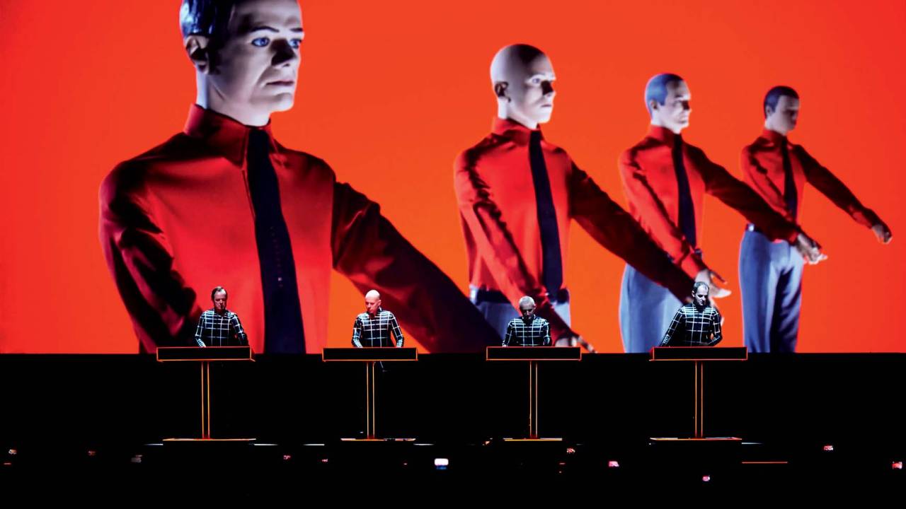 Imagem mostra quatro homens em cima de palco com uma projeção vermelha mostrando manequins enfileirados
