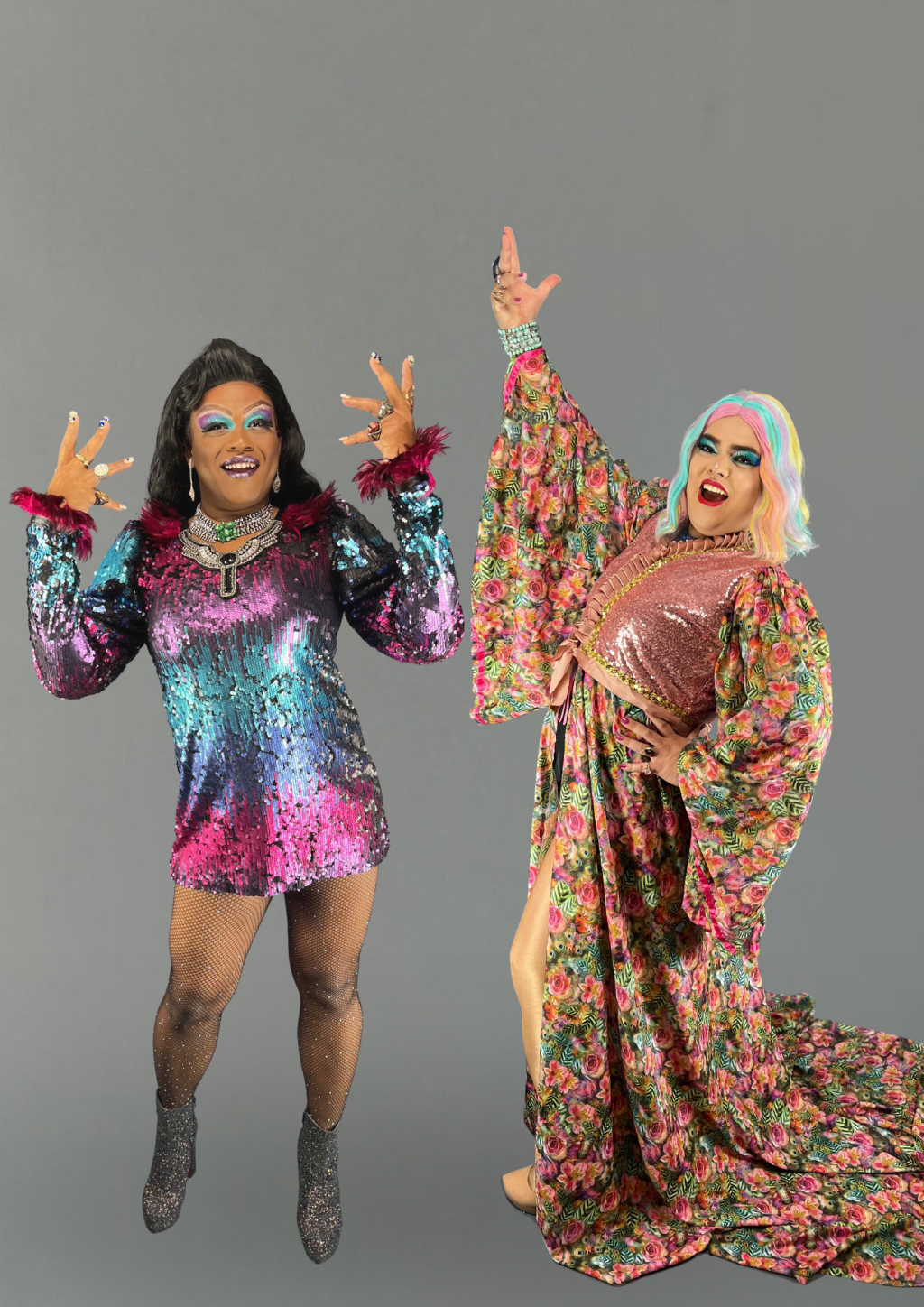 David e Bruno – Warralla Blackberry e Dhiana D’água (David Costa-Divulgação) Duas drag queens estendem as mãos e posam sorridentes. A da esquerda é negra e veste vestido nas cores roxo, azul e rosa. A da direita é branca, com peruca branca e azulada, e veste peça florida.